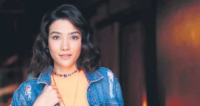 Aybüke Pusat wearing a jeans jacket with a yellow shirt and black curly hair