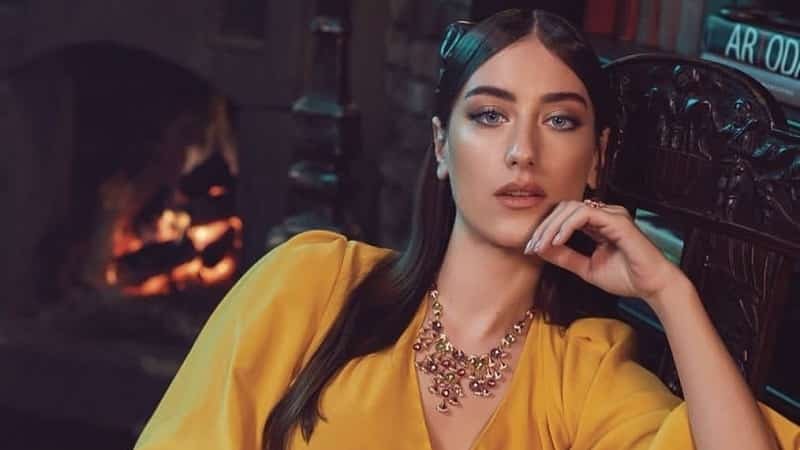 hazal kaya wearing a yellow dress with a big red necklace and long black and straight hair looking straight to camera, won lawsuit