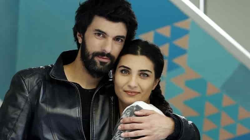Tuba Büyüküstün wearing a white t-shirt with black long hair hugged by Engin Akyürek wearing a black leather jacket
