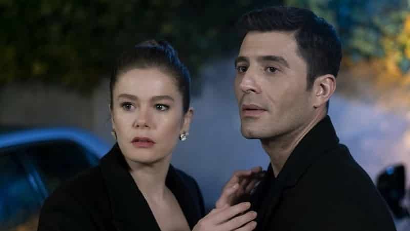 Burcu Biricik, hold Cihangir Ceyhan by the jacket both dressed in black, looking surprised, Camdaki Kız dizi series