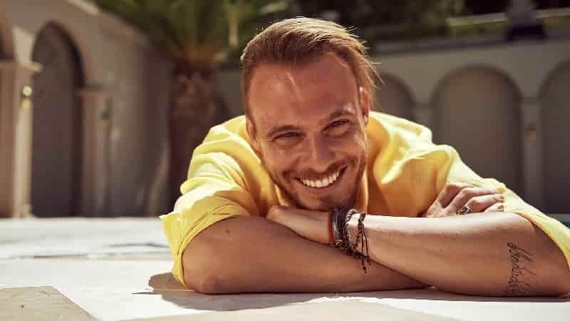 Kerem Bürsin wearing a yellow t-shirt with short blonde hair sitting with his head on his hands Kerem Bürsin