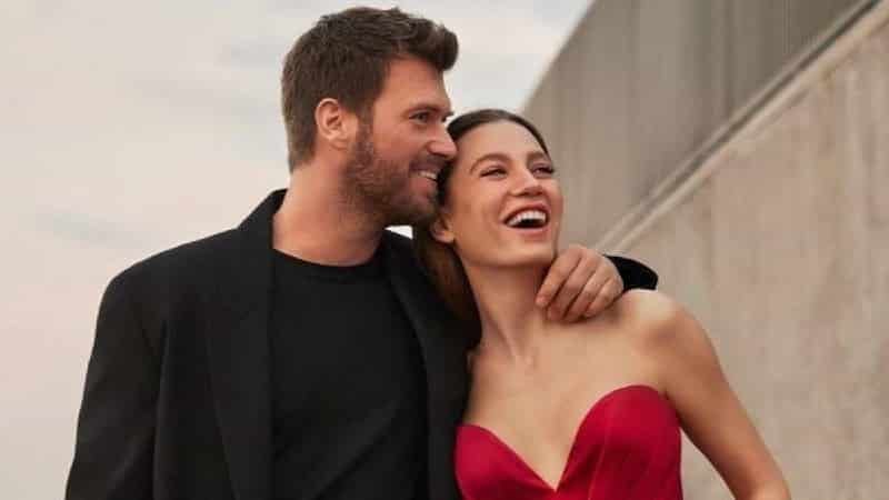 Kıvanç Tatlıtuğ wearing a black suit hugging Serenay Sarıkaya wearing a red dress and smiling in aile turkish series debut
