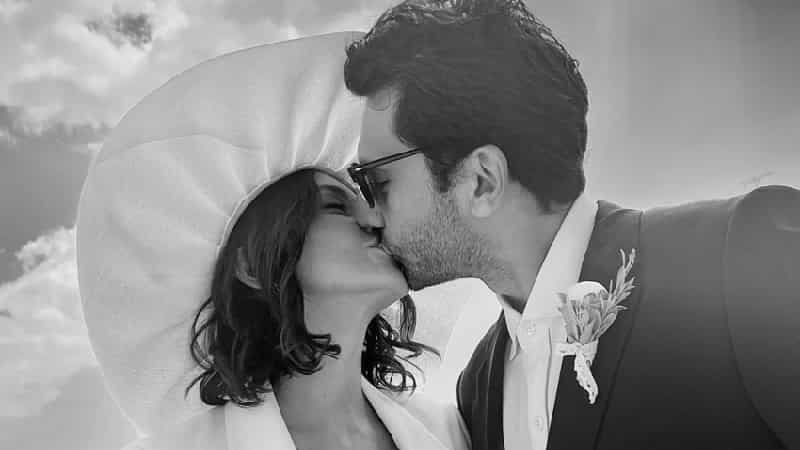 Kaan Urgancıoğlu wearing a groom suit next to his girlfriend now wife and bride Burcu Denizer wearing a big hat a white suit with a white rose bouquet, their wedding took place in athens kissing