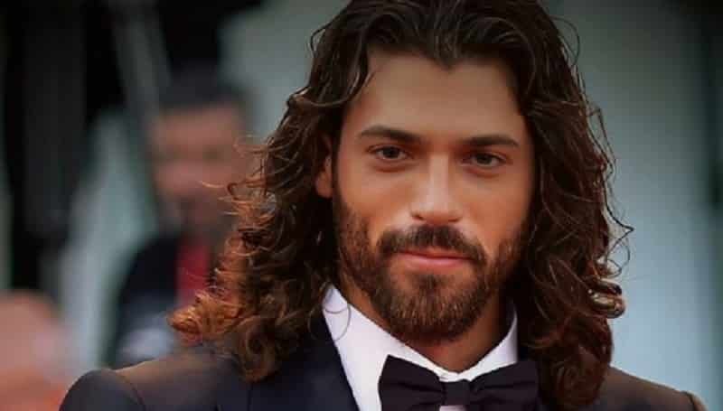 new close up Can Yaman wearing a black suit on the red carpet with long hair